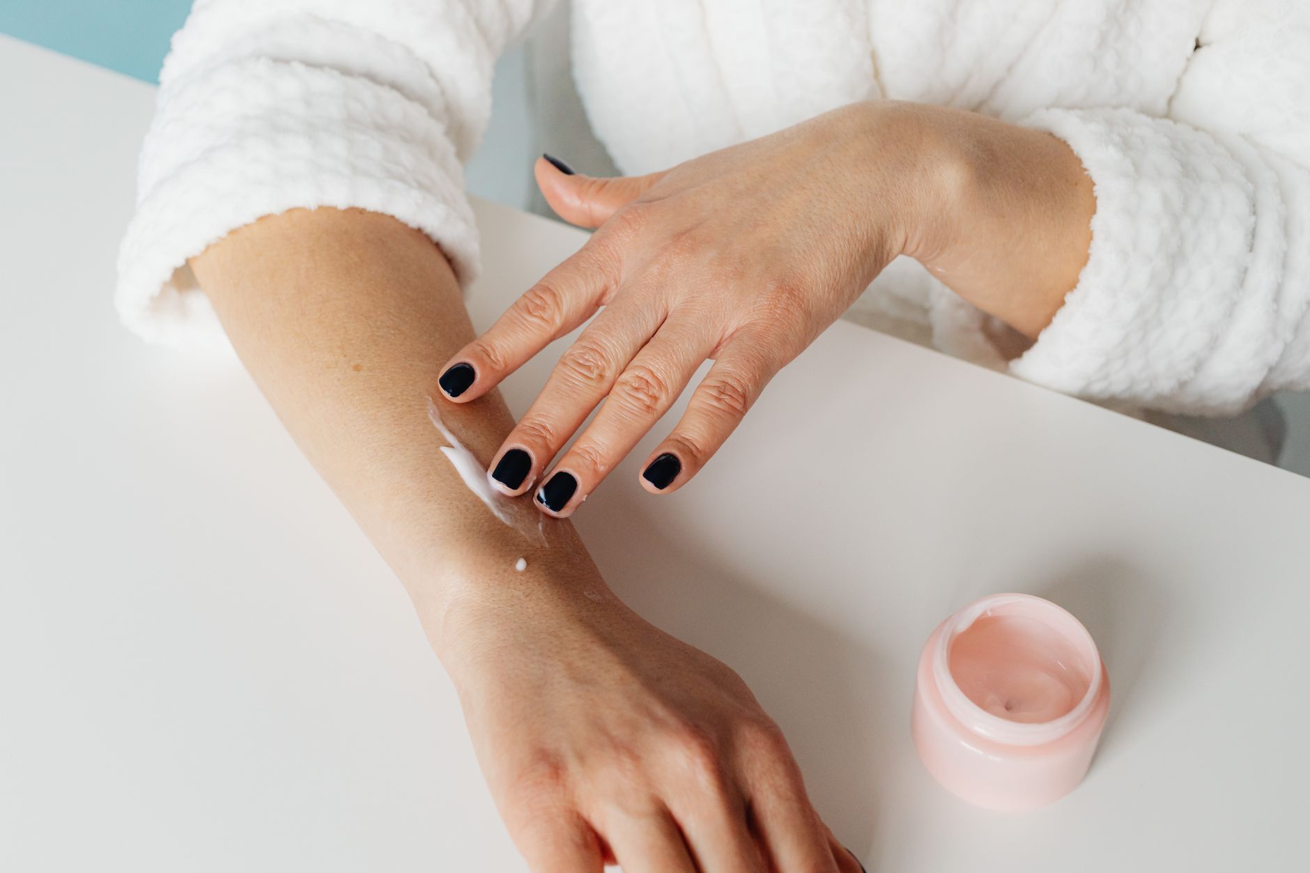 A person in a white robe smoothing cream onto the inside of their forearm at a table