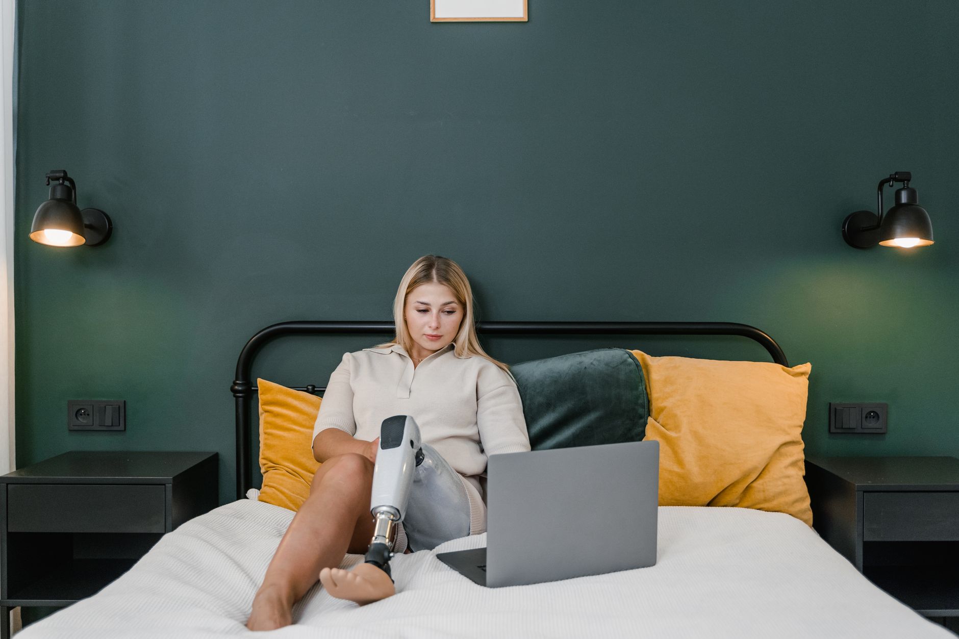 A woman with a prosthetic leg sits on her bed working on a laptop
