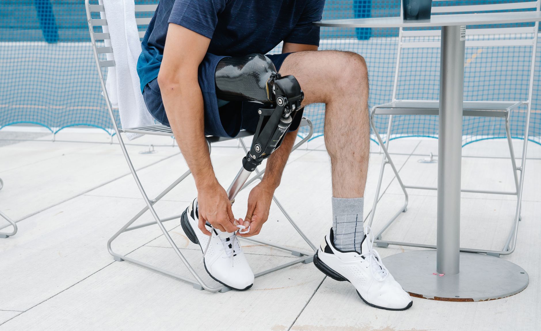 A man with a prosthetic leg sits on an outdoor chair and ties the laces of his white sneakers
